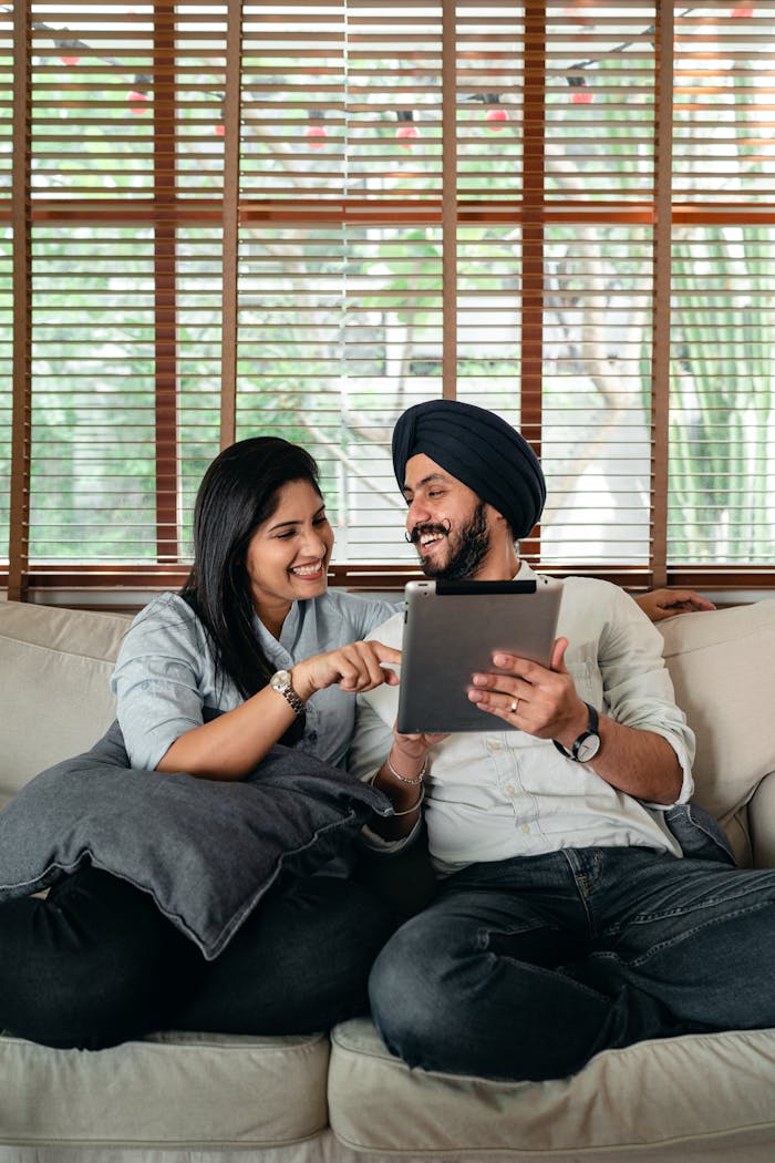 Joyful young Indian couple having fun while browsing tablet on couch